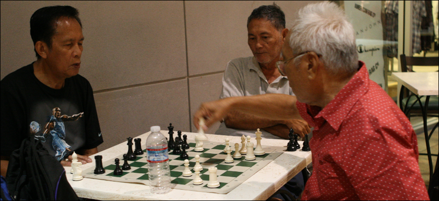 Consuelo, Bob, and Ross playing chess at Pearl Ridge Shopping Center.